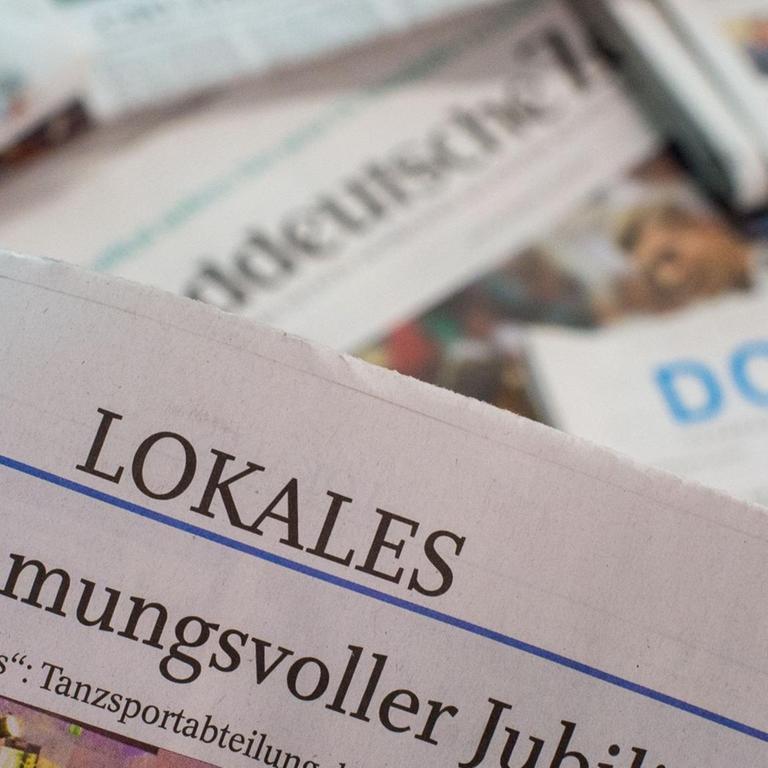 Eine Lokalzeitung wird über andere Zeitungen gehalten. Oben auf der Seite ist die Ressortbezeichnung "Lokales" zu lesen. Foto: Lino Mirgeler/dpa
