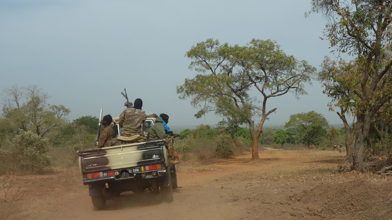 Ein Jeep mit drei bewaffneten Soldaten fährt übers Land.