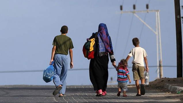 Vier Menschen, darunter zwei Kinder, gehen mit gepackten Straßen auf einer Straße.