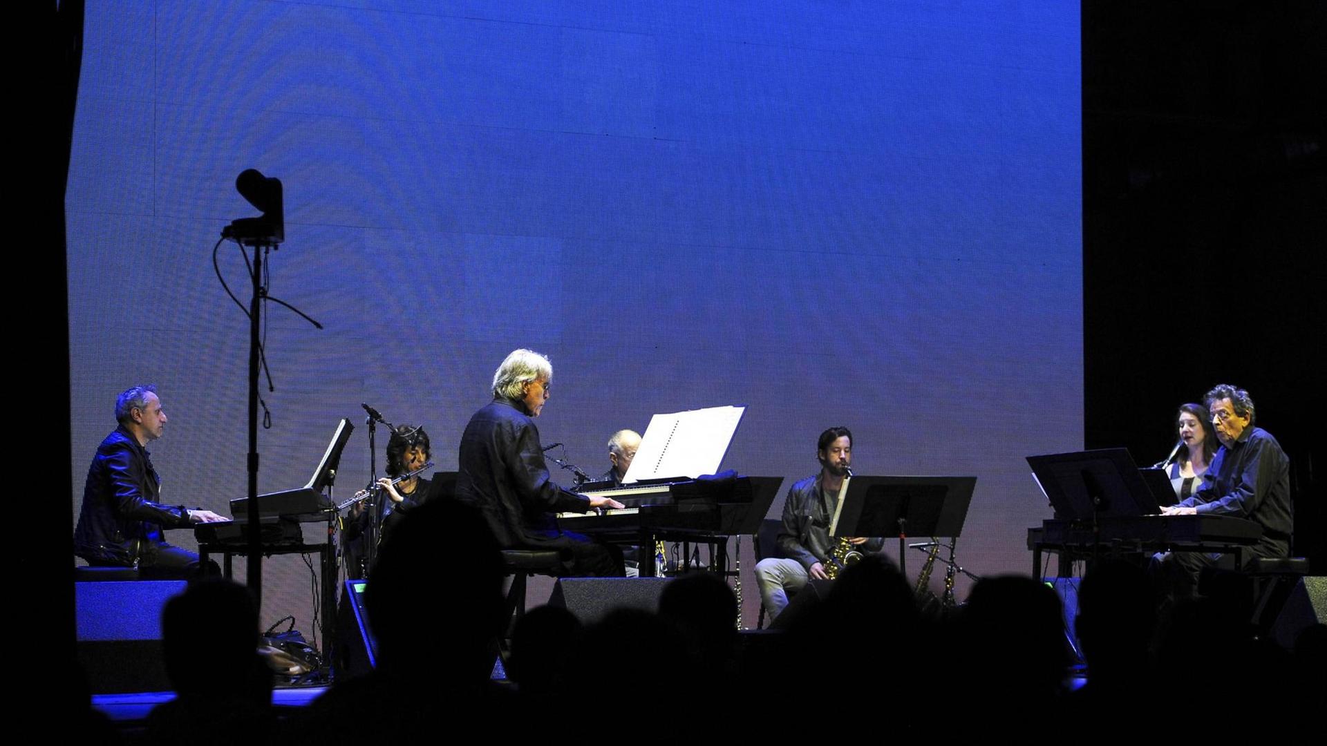 The Phillip Glass Ensemble live auf dem Day For Night Festival 2015 rund um die Silver Street Studios in Houston, 19.12.2015 Das Ensemble spielt auf der Bühne vor einer blau beleuchteten Leinwand rechts am Keyboard sitzt der Komponist und Musiker Philip Glass