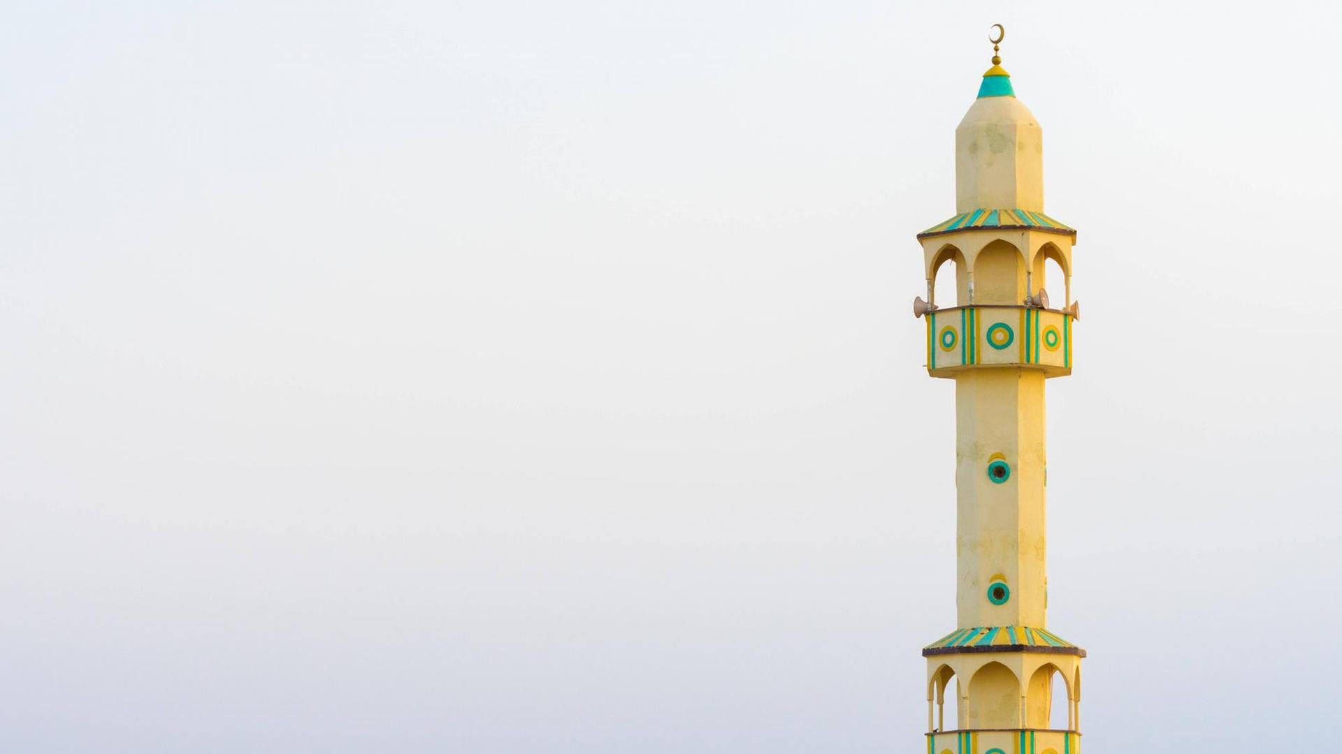 Gelbes Minarett einer somalischen Moschee vor bewölktem Himmel.
