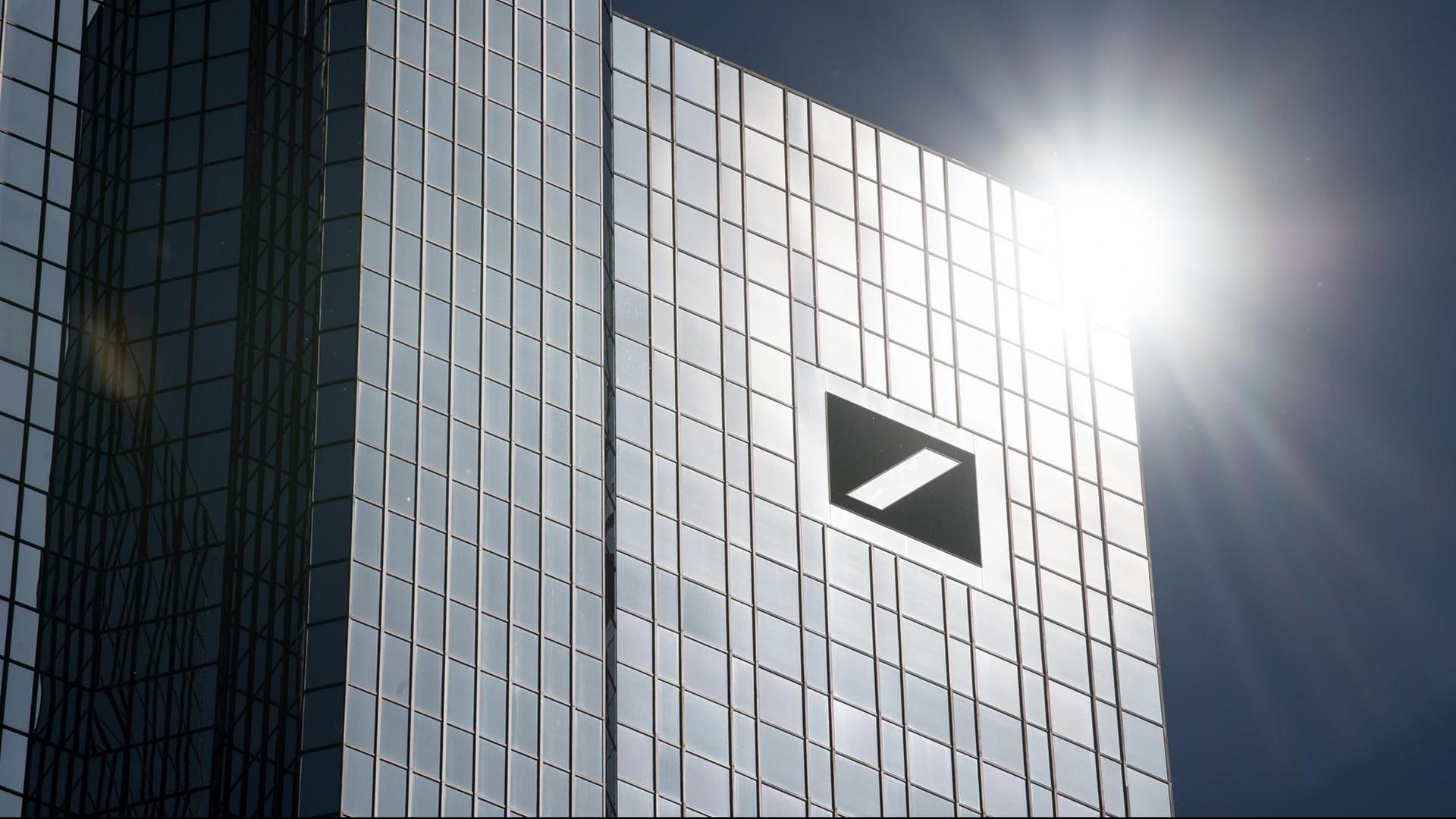 Das Gebäude der Deutschen Bank unter blauem Himmel. Die Sonne reflektiert auf der Fassade.