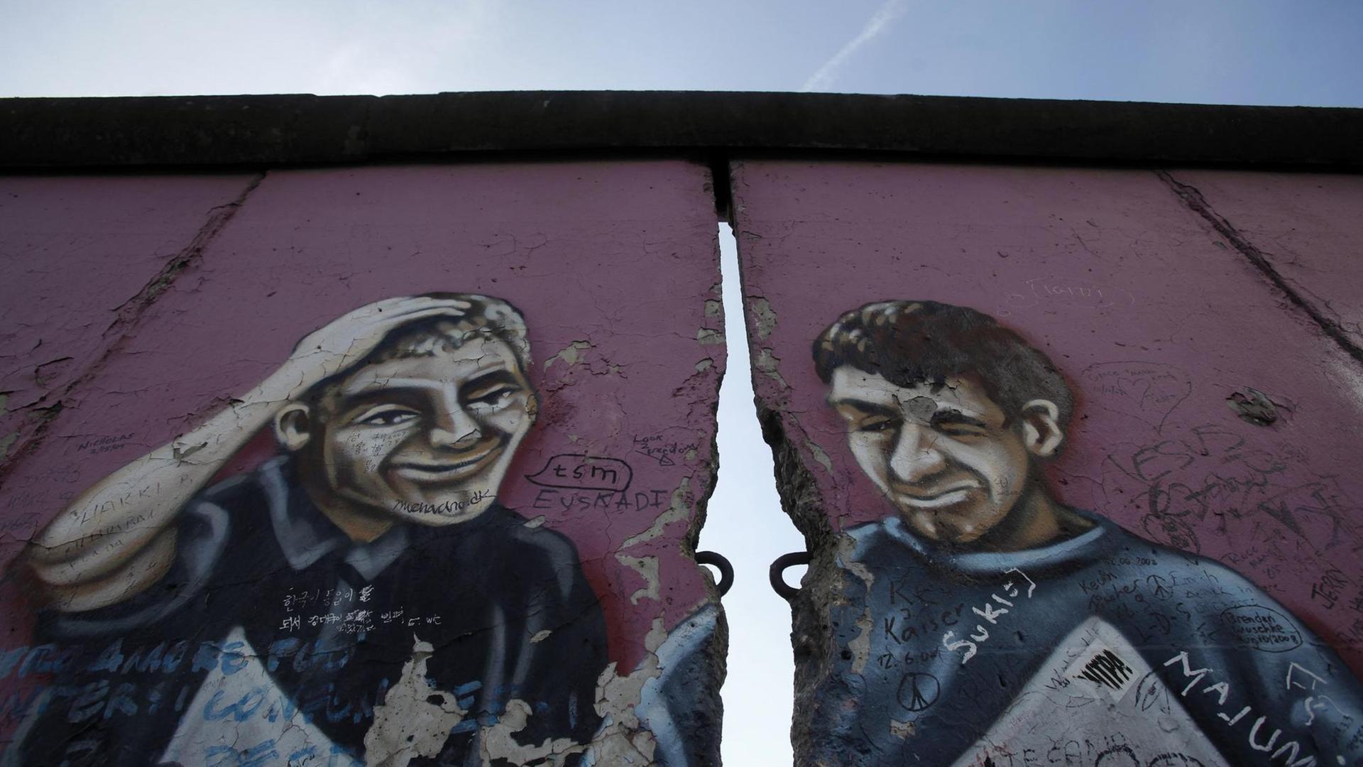 Ein ehemaliger Teil der East Side Gallery in Berlin zeigt ein Graffiti mit zwei Männern, getrennt durch einen Riss in der Mauer.