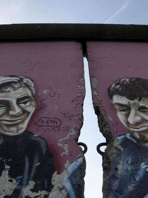 Ein ehemaliger Teil der East Side Gallery in Berlin zeigt ein Graffiti mit zwei Männern, getrennt durch einen Riss in der Mauer.