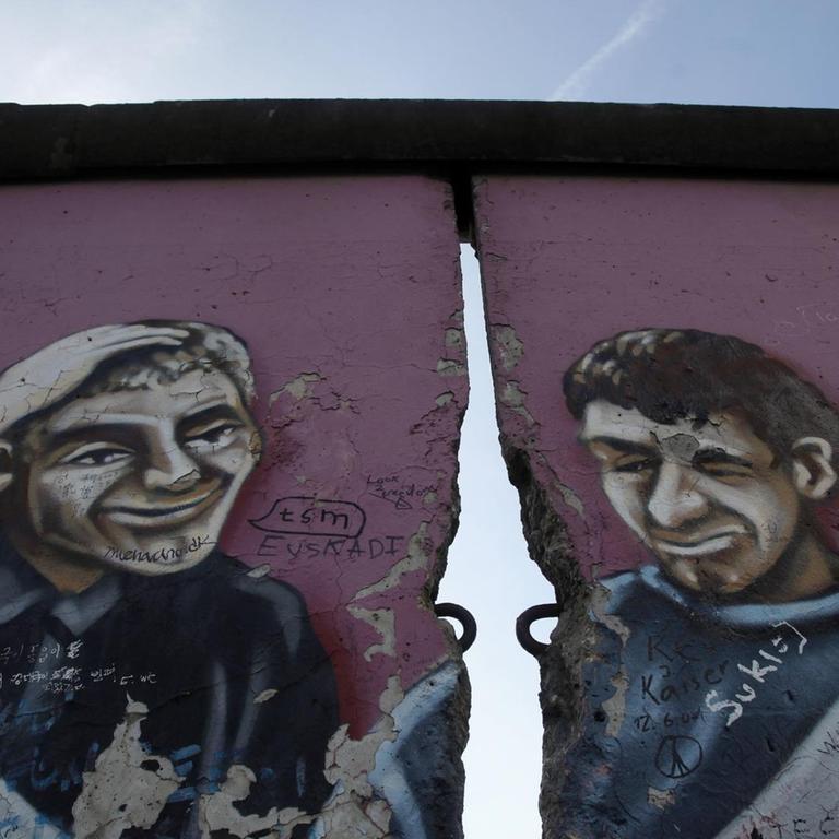 Ein ehemaliger Teil der East Side Gallery in Berlin zeigt ein Graffiti mit zwei Männern, getrennt durch einen Riss in der Mauer.