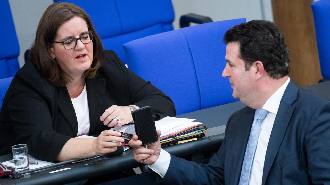 05.07.2018, Berlin: Hubertus Heil (r, SPD), Bundesminister für Arbeit und Soziales, zeigt Kerstin Griese (SPD), Parlamentarische Staatssekretärin beim Bundesminister für Arbeit und Soziales, bei der Plenarsitzung im Deutschen Bundestag etwas auf seinem Smartphone. Höhepunkt der 46. Sitzung der 19. Wahlperiode ist die Verabschiedung des Bundeshaushalts. Zuvor berät das Parlament in seiner letzten Sitzung vor der Sommerpause mehrere Einzeletats. Foto: Bernd von Jutrczenka/dpa | Verwendung weltweit