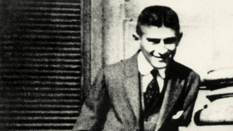 Franz Kafka steht mit verletztem Daumen am Eingangsportal des Oppelthauses am Altstädter Ring in Prag, welches ab 1913 das Wohnhaus der Familie Kafka war (Foto, um 1914).