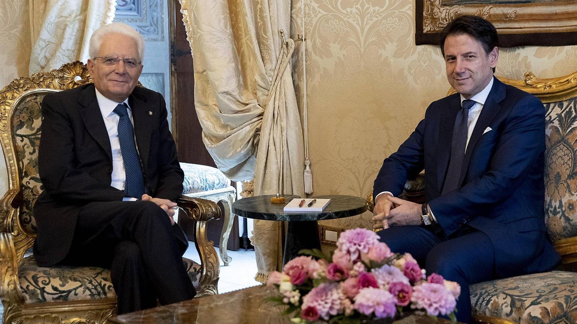 Italiens Staatspräsident Mattarella und Ministerpräsident Conte sitzen sich auf Stühlen gegenüber.