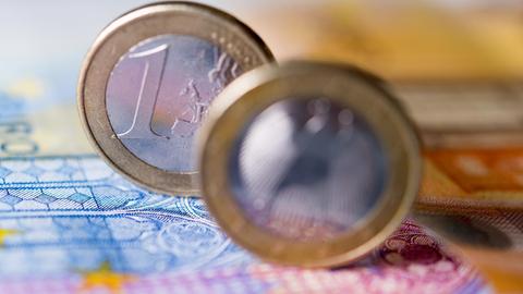 Zwei Ein-Euro-Münzen stehen auf einem Geldschein.