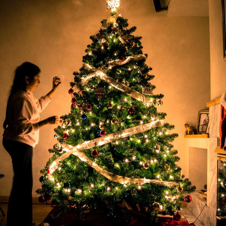 Eine Frau schmückt einen leuchtenden Weihnachtsbaum.