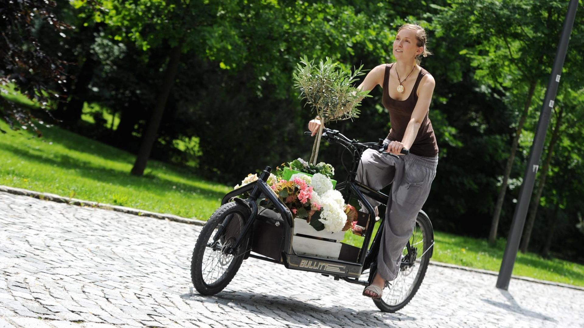 Eine Frau fährt mit einem Transportrad, das mit Blumen beladen ist. Mit Denkfabrik-Stempel