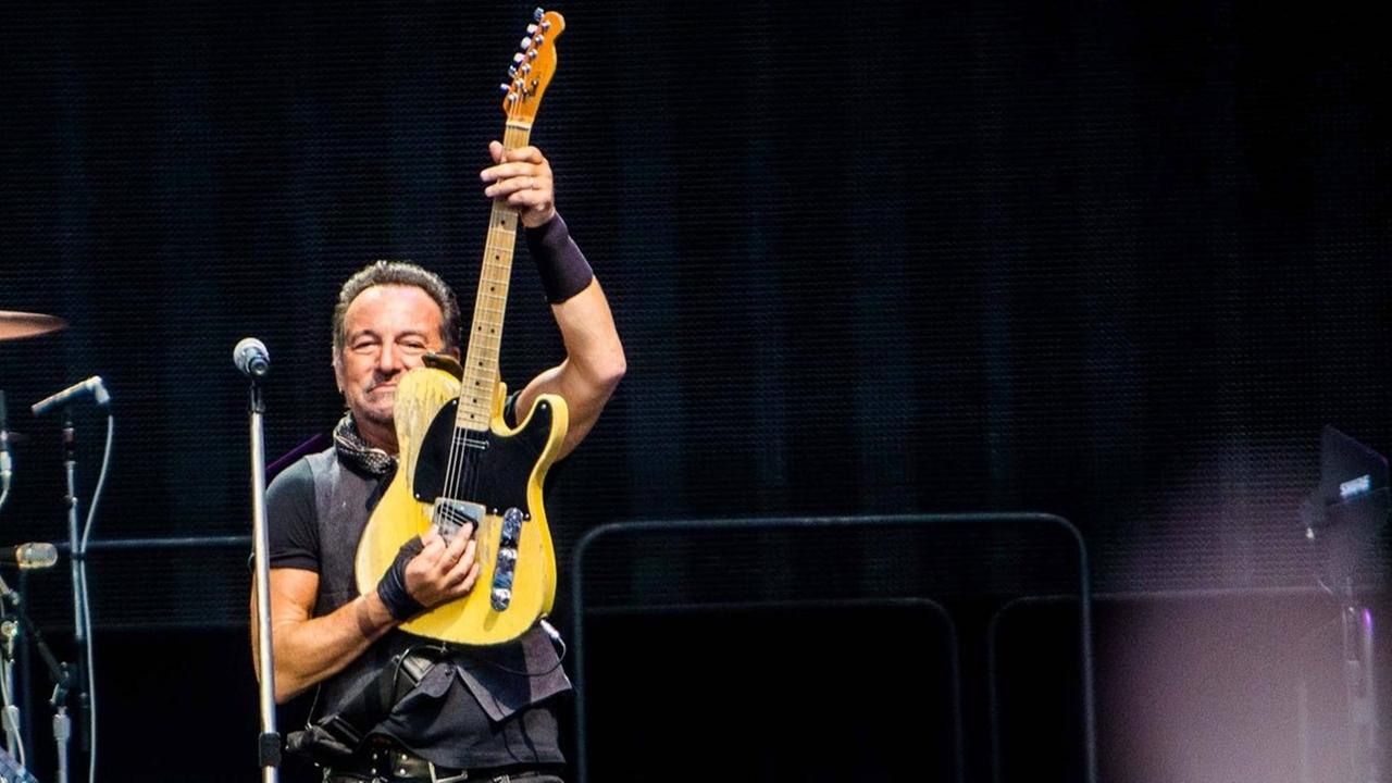 Bruce Sprungsteen mit The E Street Band auf der Bühne in Mailand: Er spielt seine Gitarre senktrecht, im Hintergrund ist sein Schlagzeuger zu sehen.