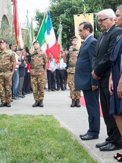 Steinmeier, Mogherini und Minchetti stehen an einem Grab, im Hintergrund salutieren Soldaten.