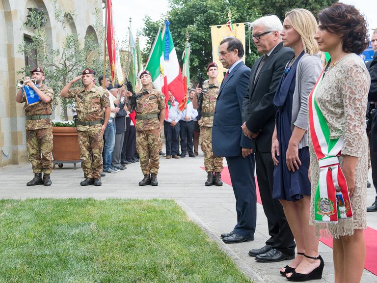 Steinmeier, Mogherini und Minchetti stehen an einem Grab, im Hintergrund salutieren Soldaten.