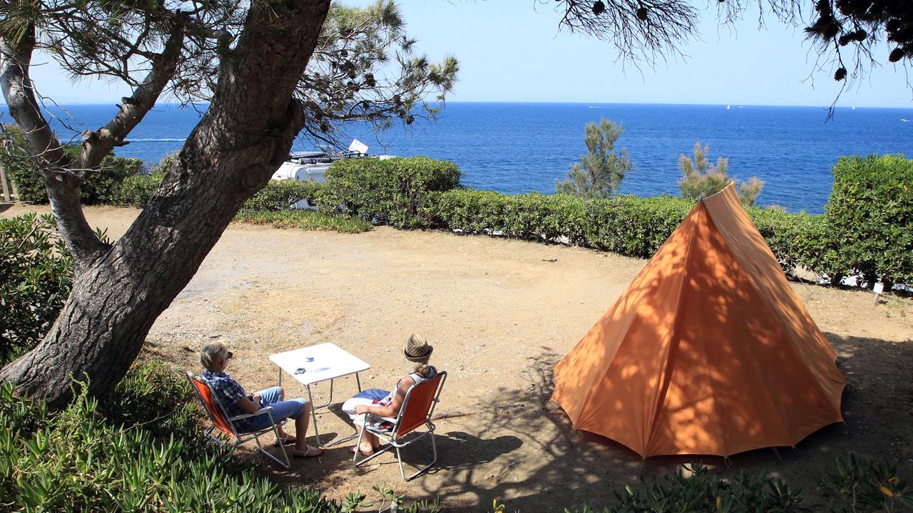 Camper sitzen an einem Tisch neben ihrem Zelt mit Blick auf den See auf einem Zeltplatz.