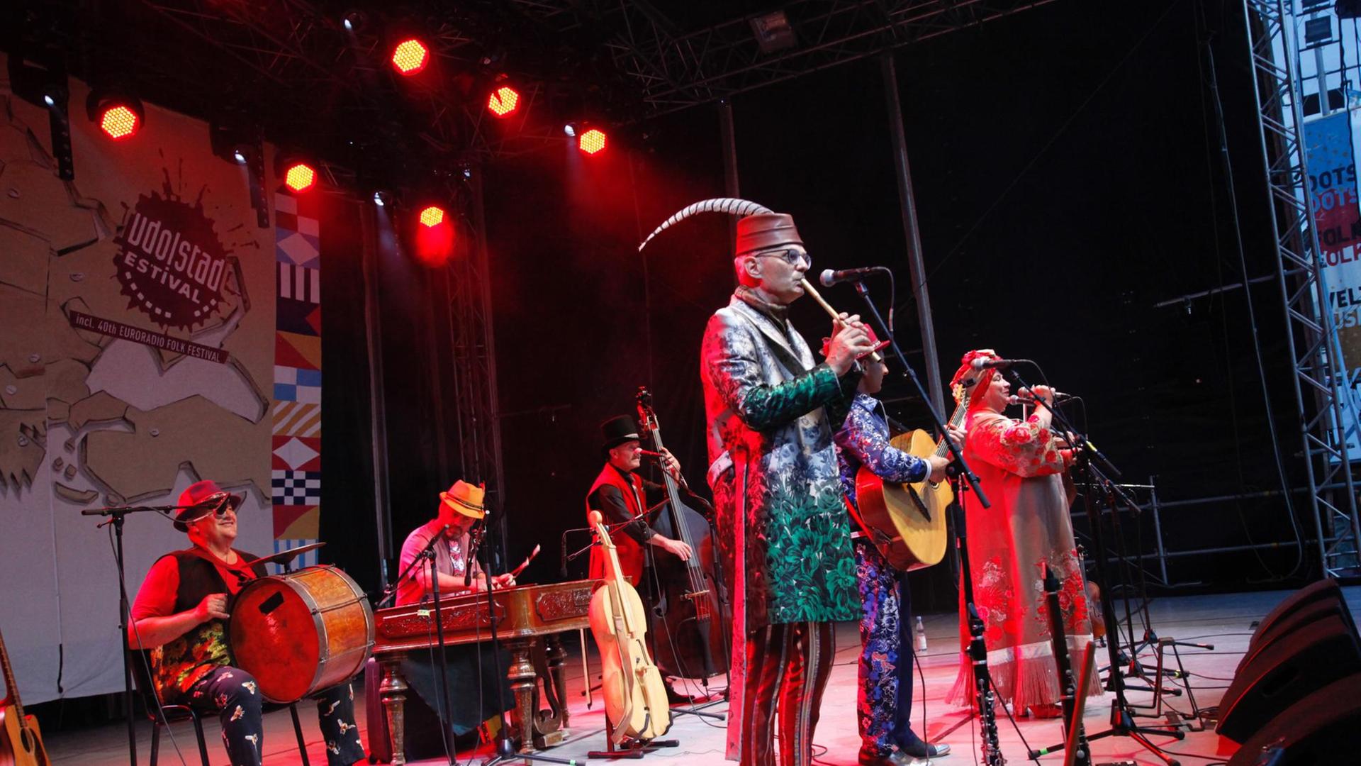 Vier buntgekleidete Musiker und eine Sängerin stehen auf einer Bühne.