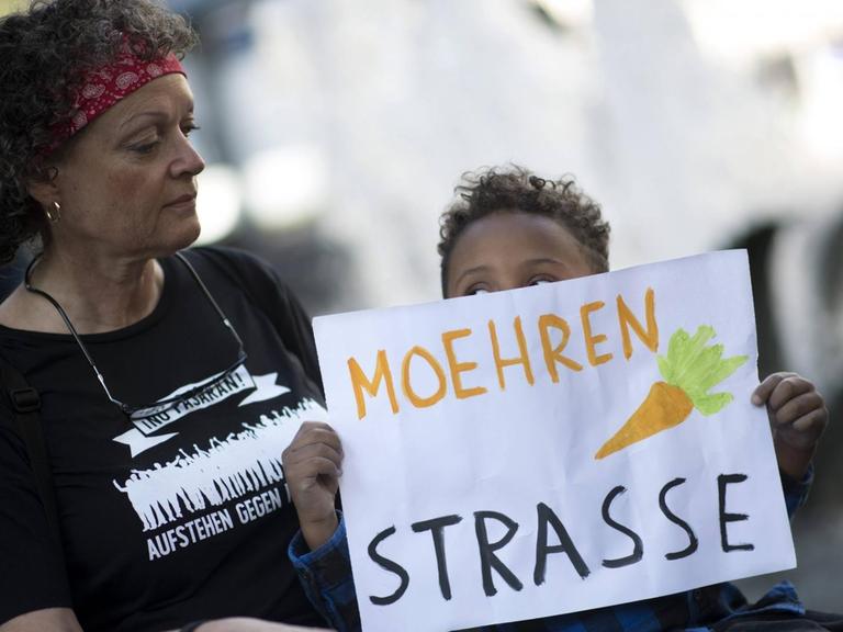 Ein Kind hält ein Schild mit einer gemalten Möhre über dem Text "Moehrenstraße" hoch, anlässlich des Umbenennungsfestes von Mohrenstraße zu Anton W Amo Strasse