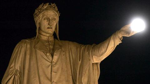 Der Vollmond scheint als leuchtende Kugel auf der Hand einer Dante-Statue zu liegen.