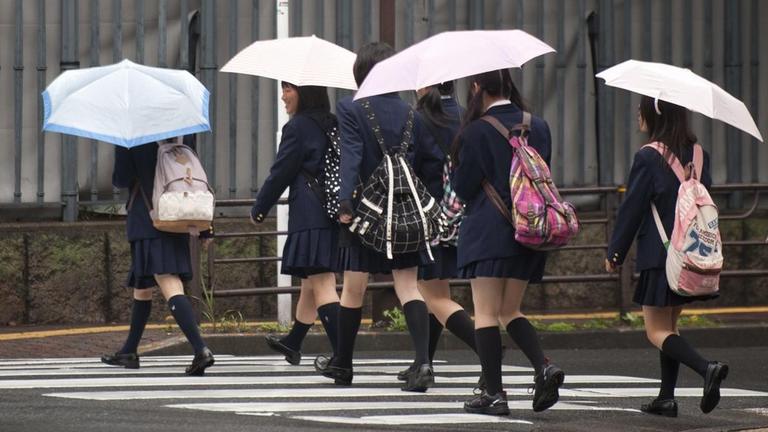 Schülerinnen in Japan. Mädchen gekleidet in Schuluniform überqueren einen Zebrastreifen.