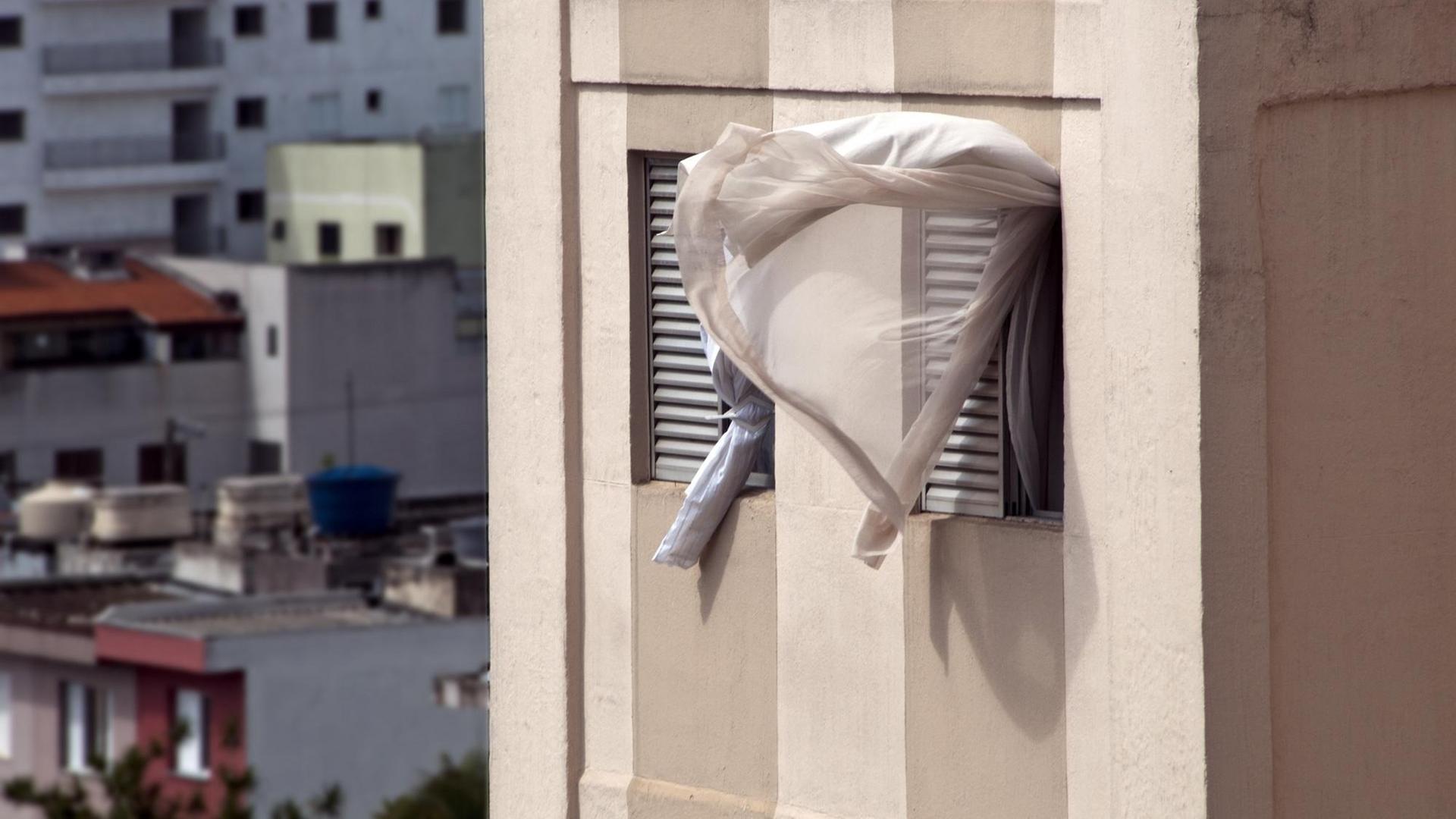 Ein Vorhang weht aus einem offenem Fenster.