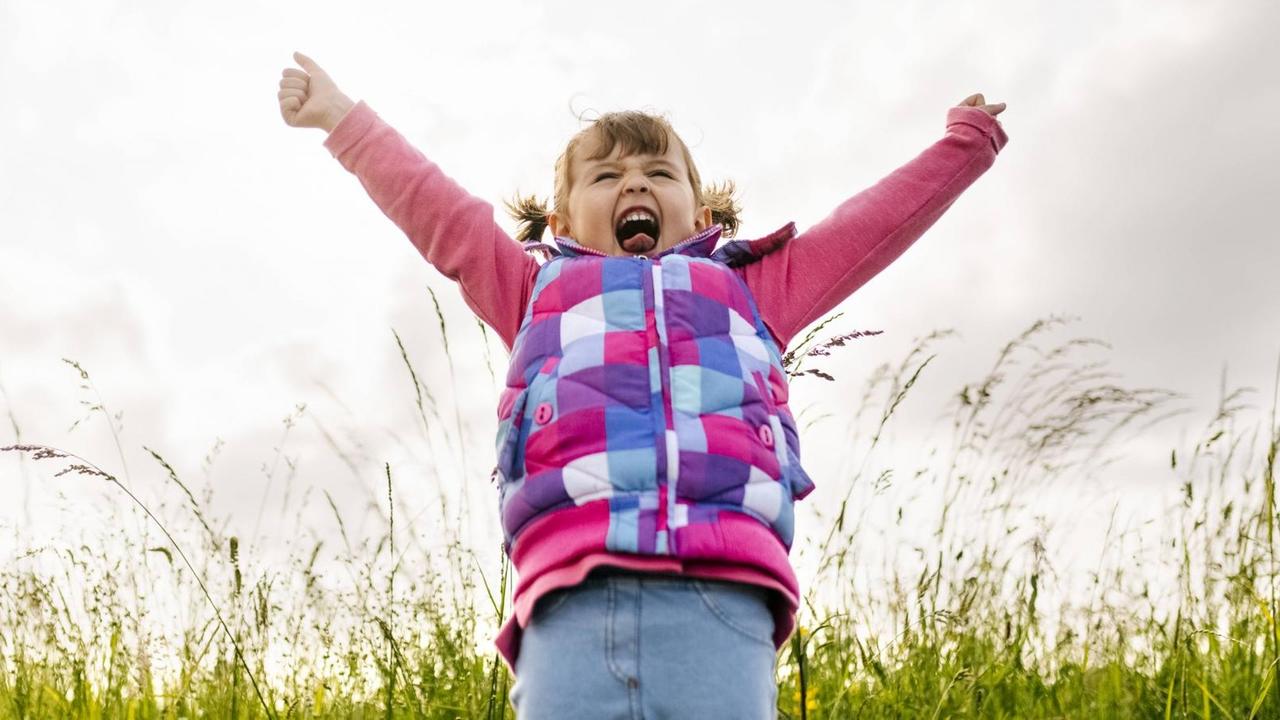 Ein kleines Mädchen wirft vor Freude die Arme in die Luft.