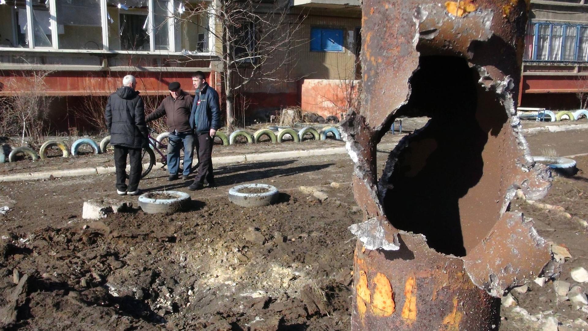 Männer stehen in einer offenbar durch Waffenbeschuss zerstörten Gegend in Donezk.