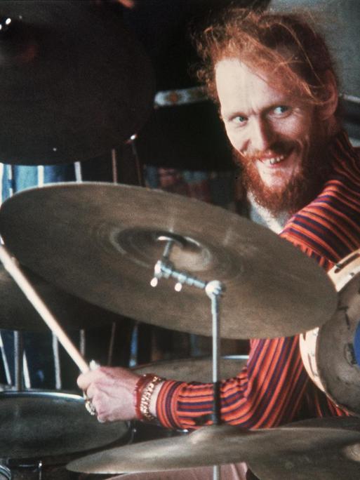 Ginger Baker sitzt am Schlagzeug und grinst.