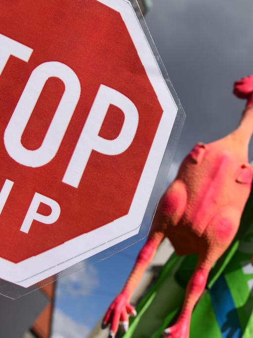 Demonstranten mit einem Schild, auf dem "Stop TTIP" steht, und gerupften Gummihühnern an einem Ast.
