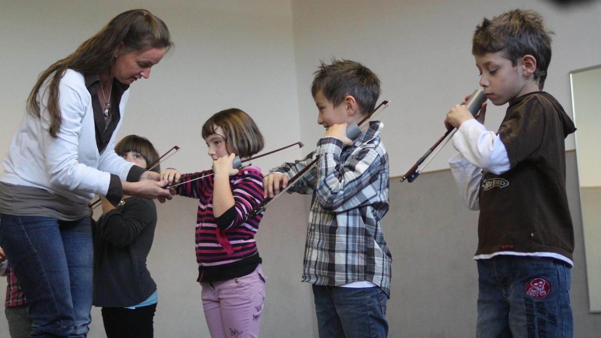 Eine Frau hilft vier Kindern beim Stimmen ihrer Geigen.