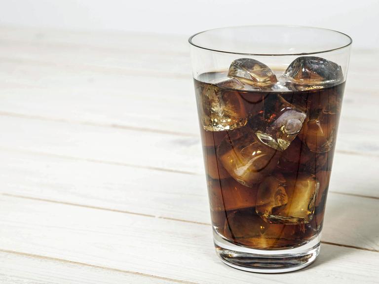 Ein Glas mit Cola steht auf einem Holztisch.