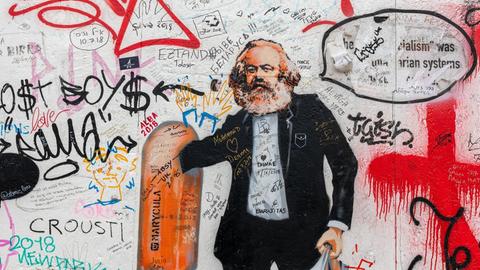Eine Street-Art-Karikatur an einer Wand zeigt Karl Marx als Flaschensammler, der in einem Mülleimer wühlt.