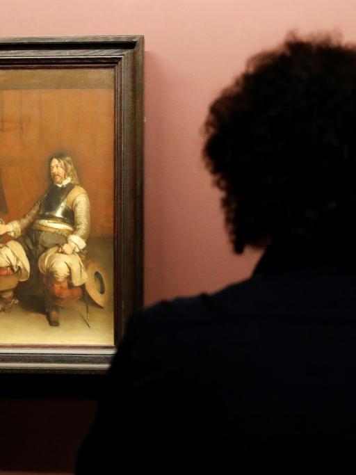 Man sieht die Silhouette eines Mannes, der sich im Pariser Louvre ein Gemälde von Gerard ter Borch anschaut.