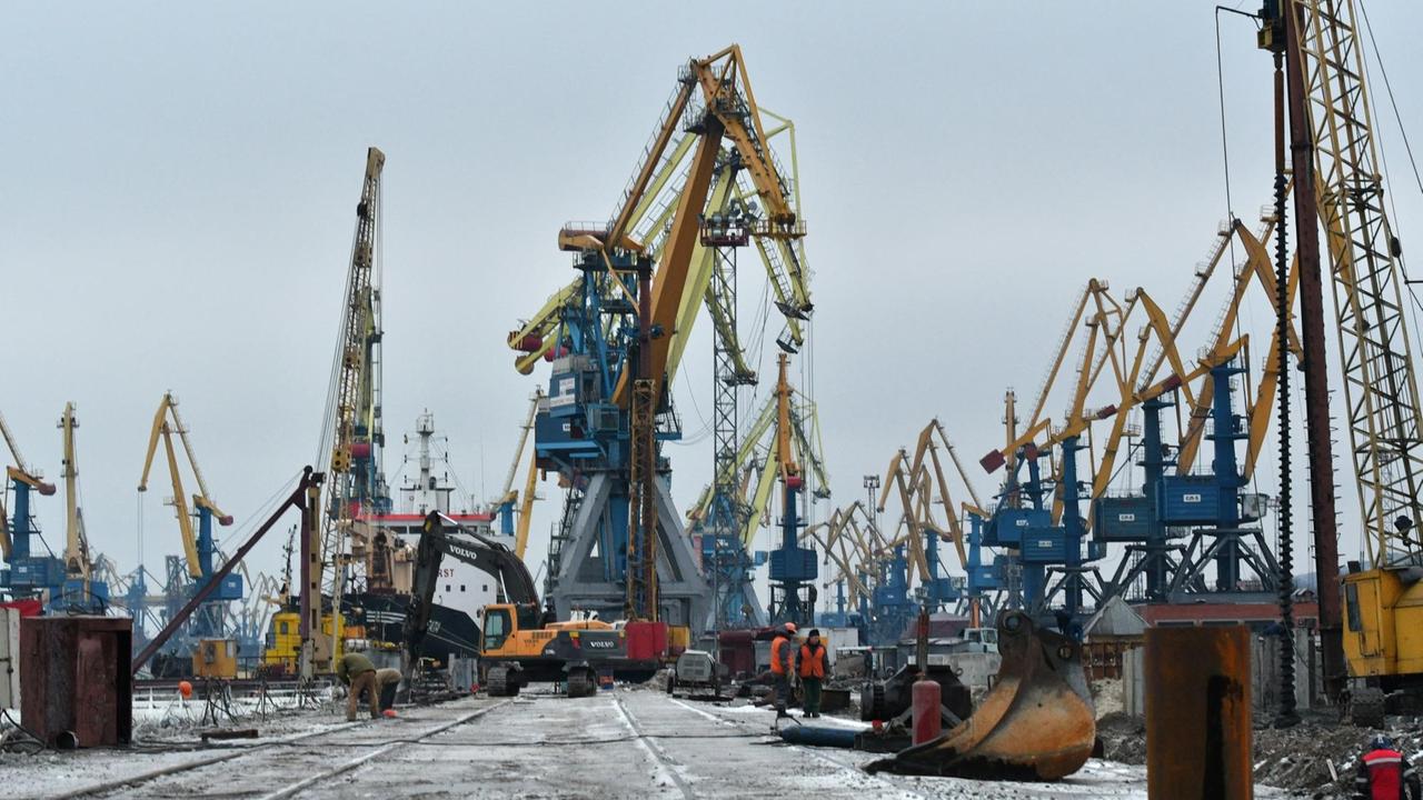 Hafenarbeiter errichten ein neues Hafenterminal, im Hintergrund ragen Lastenkräne in die Höhe.