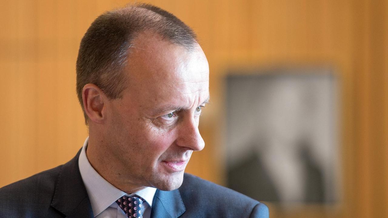 Merz' Gesicht wird vom Tageslicht auf der linken Hälfte hell angestrahlt. Hinter ihm sieht man eine braune Wand.