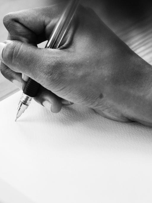 Eine Männerhand ist zu sehen, die einen Stift hält und dabei ist, etwas in einem leeren Buch zu notieren.