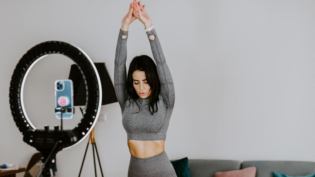 Frau macht Yogaübungen vor Smartphone auf Stativ mit Ringlicht