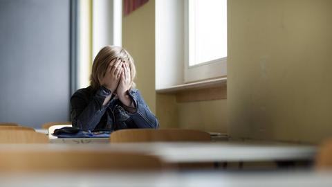 Ein Schüler sitzt allein im Klassenraum und hält sich die Hände vors Gesicht