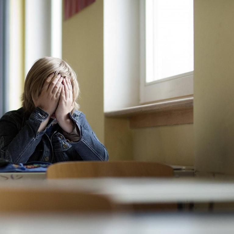 Ein Schüler sitzt allein im Klassenraum und hält sich die Hände vors Gesicht
