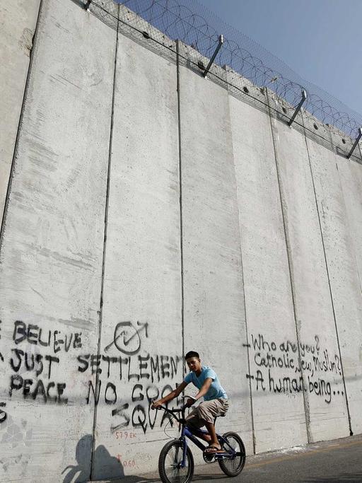 Ein arabischer Junge fährt im arabischen Teil in Ost-Jerusalem an der Mauer entlang, die den israelischen vom palästinensischen Teil trennt.