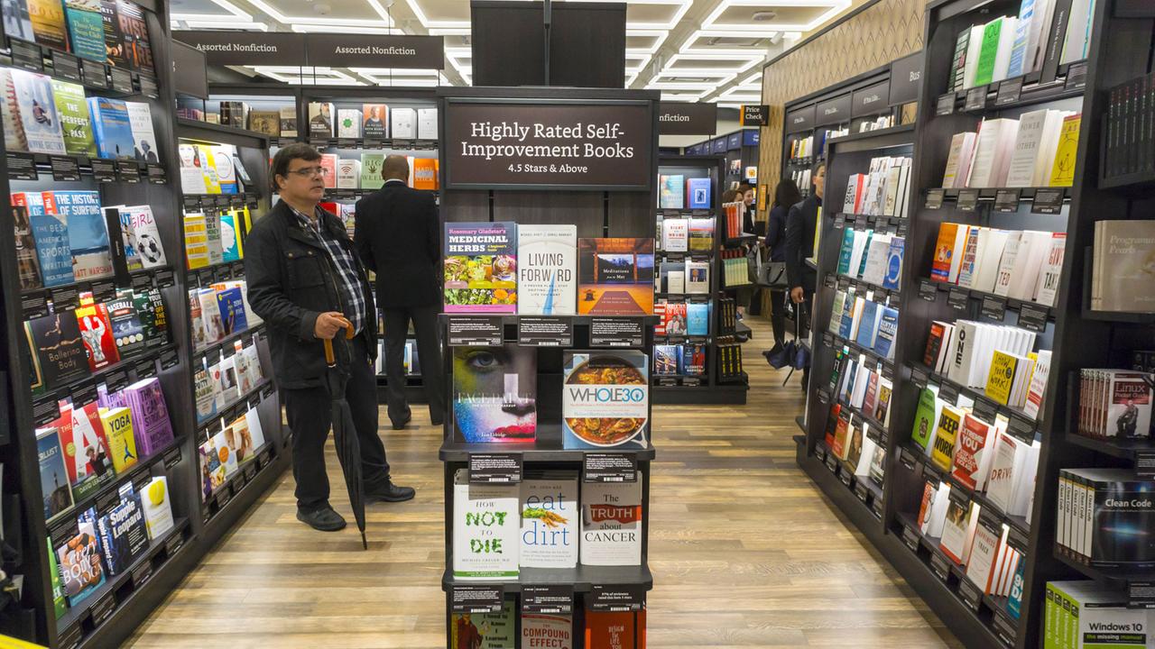 Kunden stehen vor den Regalen im New Yorker Buchladen von Amazon. Im Vordergrund ein Regel mit Ratgebern zur Selbstoptimierung, die von Onlinekäufern gut bewertet wurden.