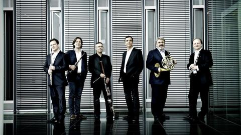 Das Ensemble Les Vents Francais posiert mit Instrumenten vor einer Fensterfront