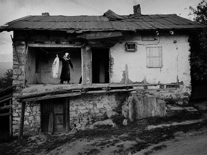 Eine Frau steht im ersten Stock eines halb verfallenen Hauses.