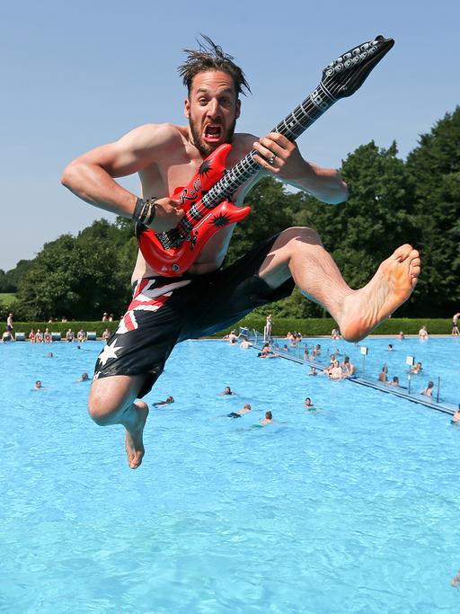Ein Mann springt mit einer aufblasbaren Gitarre vom Drei-Meter-Turm ins Wasser. 
