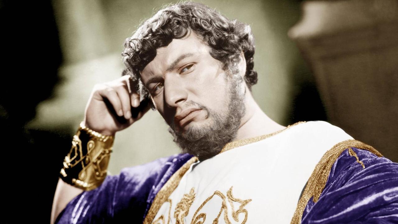 Ein Film-Still zeigt den Schauspieler Peter Ustinov als Kaiser Nero in purpurnem Gold-verzierten Gewand den Kopf nachdenklich auf die rechte Hand gestützt