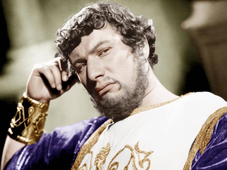 Ein Film-Still zeigt den Schauspieler Peter Ustinov als Kaiser Nero in purpurnem Gold-verzierten Gewand den Kopf nachdenklich auf die rechte Hand gestützt
