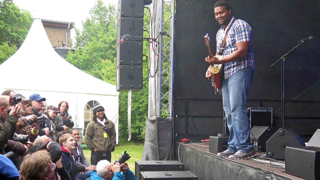 Ein Gitarrist steht am Bühnenrand und spielt, vor ihm Zuschauer und Fotografen.