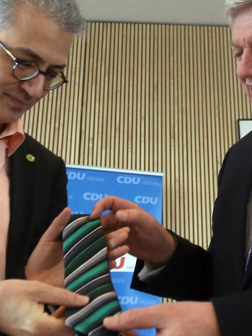 Der Ministerpräsident von Hessen, Volker Bouffier (CDU, r), überreicht dem Vorsitzenden von Bündnis 90/Die Grünen in Hessen, Tarek Al-Wazir (l), eine schwarz-grüne Krawatte.