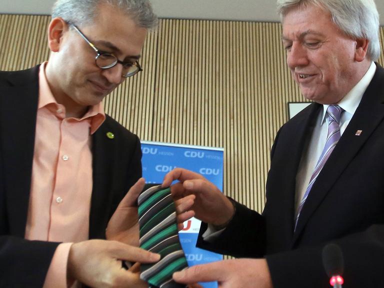 Der Ministerpräsident von Hessen, Volker Bouffier (CDU, r), überreicht dem Vorsitzenden von Bündnis 90/Die Grünen in Hessen, Tarek Al-Wazir (l), eine schwarz-grüne Krawatte.