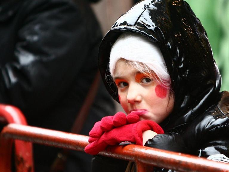 Ein kleines Mädchen zieht eine Schnute, während es im Regen auf den Start des Rosenmontagszuges wartet.