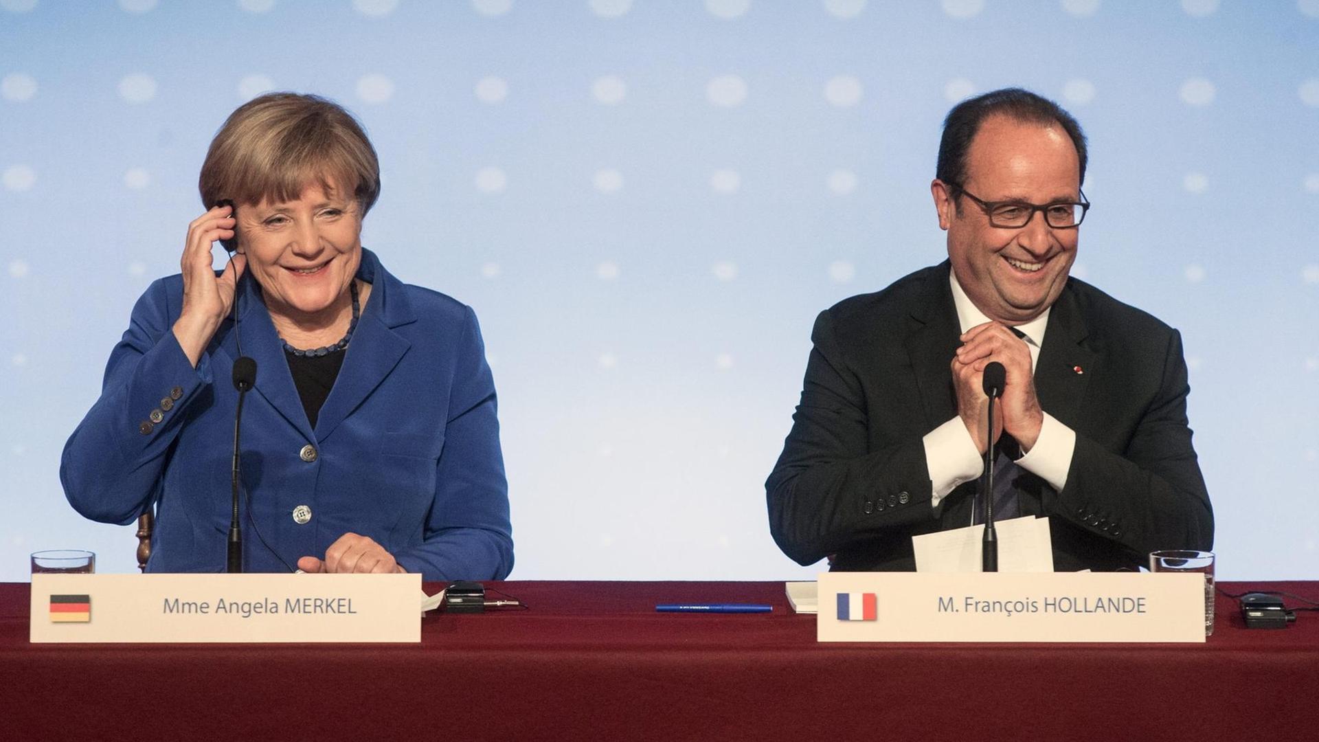 Bundeskanzlerin Angela Merkel und Frankreichs Präsident Francois Hollande geben nach dem Ukraine-Gipfel eine Pressekonferenz. Sie sitzen hinter einem Pult und grinsen.